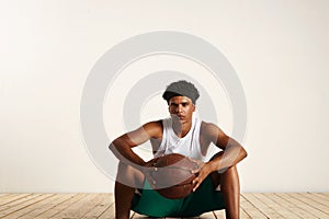 Handsome young black basketball player sitting on the wooden floor