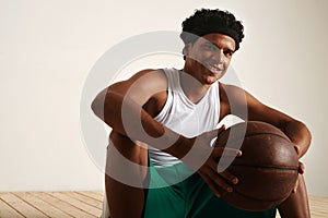 Handsome young black basketball player sitting on the wooden floor