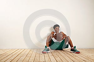 Handsome young black basketball player sitting on the wooden floor