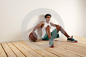 Handsome young black basketball player sitting on the wooden floor