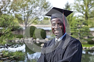 Handsome young black college graduate wearing cap and gown smiles proudly