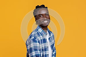 Handsome young black man with braided hair standing half-turned on yellow background