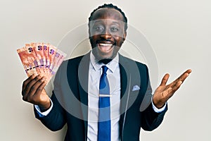 Handsome young black man holding south african rand banknotes celebrating achievement with happy smile and winner expression with