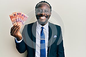 Handsome young black man holding south african rand banknotes looking positive and happy standing and smiling with a confident