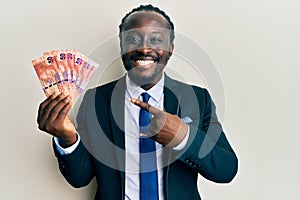 Handsome young black man holding south african rand banknotes smiling happy pointing with hand and finger