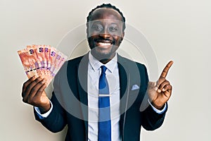 Handsome young black man holding south african rand banknotes smiling happy pointing with hand and finger to the side
