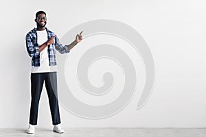 Handsome young black man pointing aside at copy space for your advertisement against white studio wall