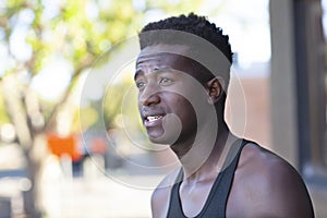 A handsome young black man stands in a street with defocused background on sunny afternoon