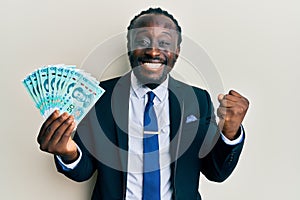 Handsome young black man wearing business suit holding 50 yuan banknotes screaming proud, celebrating victory and success very