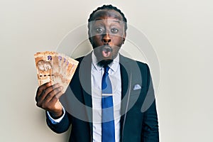 Handsome young black man wearing business suit holding 20 rands banknotes scared and amazed with open mouth for surprise, photo