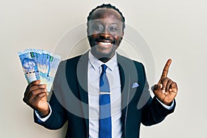 Handsome young black man wearing business suit holding 100 rands banknotes smiling happy pointing with hand and finger to the side