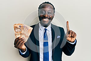 Handsome young black man wearing business suit holding 20 rands banknotes smiling with an idea or question pointing finger with photo