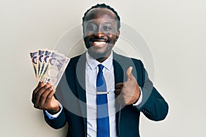 Handsome young black man wearing business suit holding yens banknotes smiling happy and positive, thumb up doing excellent and