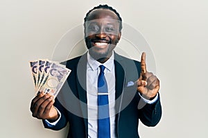 Handsome young black man wearing business suit holding yens banknotes smiling with an idea or question pointing finger with happy