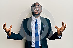 Handsome young black man wearing business suit and tie crazy and mad shouting and yelling with aggressive expression and arms
