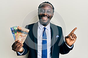 Handsome young black man wearing business suit and tie holding canadian dollars smiling happy pointing with hand and finger to the