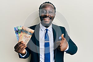 Handsome young black man wearing business suit and tie holding canadian dollars smiling happy and positive, thumb up doing