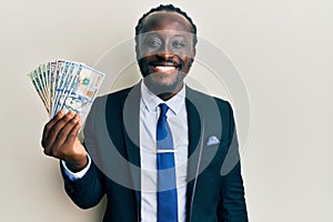 Handsome young black man wearing business suit and tie holding dollars looking positive and happy standing and smiling with a