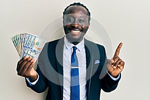 Handsome young black man wearing business suit and tie holding dollars smiling happy pointing with hand and finger to the side