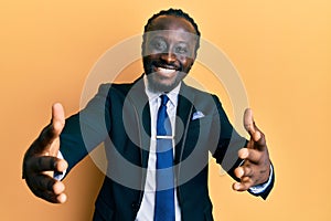 Handsome young black man wearing business suit and tie looking at the camera smiling with open arms for hug