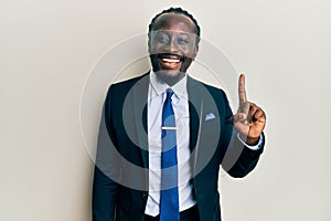 Handsome young black man wearing business suit and tie pointing finger up with successful idea