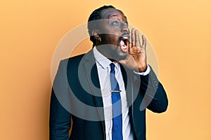 Handsome young black man wearing business suit and tie shouting and screaming loud to side with hand on mouth