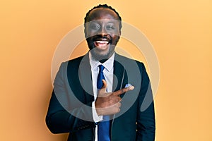 Handsome young black man wearing business suit and tie smiling cheerful pointing with hand and finger up to the side