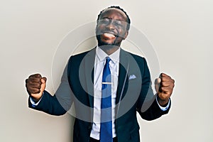 Handsome young black man wearing business suit and tie very happy and excited doing winner gesture with arms raised, smiling and