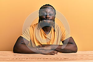 Handsome young black man wearing casual clothes sitting on the table puffing cheeks with funny face