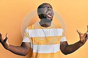 Handsome young black man wearing casual yellow tshirt crazy and mad shouting and yelling with aggressive expression and arms