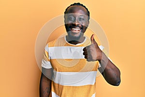 Handsome young black man wearing casual yellow tshirt smiling happy and positive, thumb up doing excellent and approval sign