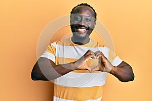 Handsome young black man wearing casual yellow tshirt smiling in love showing heart symbol and shape with hands