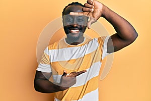 Handsome young black man wearing casual yellow tshirt smiling making frame with hands and fingers with happy face
