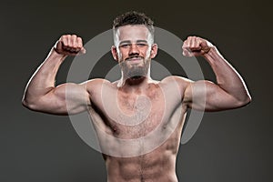 Handsome young body builder flexing biceps, on grey background