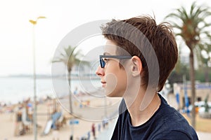 Handsome young boy wearing glasses looking at sea over panorama of Alicante. Beautiful calm smiling teen boy at Mediterranean