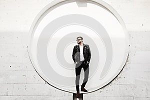 A handsome young brutal men, stylish and fashionable man with beard, in leather jacket black jeans and black sunglasses