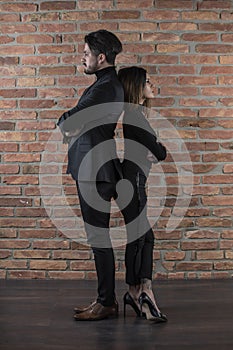 Handsome young business couple standing back to back in front of a brick wall