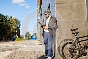 Handsome young business man in suit with a bicycle using smartphone on city street.