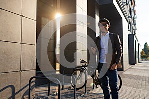 Handsome young business man in suit with a bicycle using smartphone on city street.