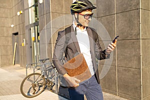 Handsome young business man in suit with a bicycle using smartphone on city street.