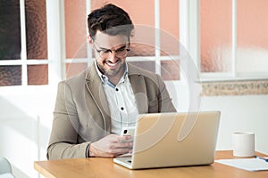 Handsome young business man using his smartphone while working with laptop in the office