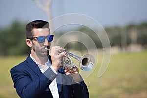 Handsome young businessman with a beard and a blue suit playing the trumpet. The man is a musician in his spare time and music is