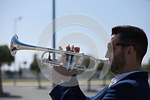 Handsome young businessman with a beard and a blue suit playing the trumpet. The man is a musician in his spare time and music is