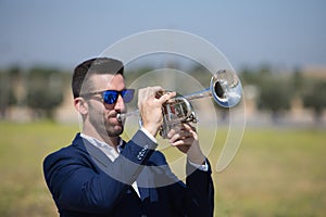 Handsome young businessman with a beard and a blue suit playing the trumpet. The man is a musician in his spare time and music is
