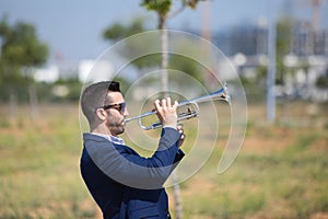 Handsome young businessman with a beard and a blue suit playing the trumpet. The man is a musician in his spare time and music is