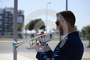 Handsome young businessman with a beard and a blue suit playing the trumpet. The man is a musician in his spare time and music is