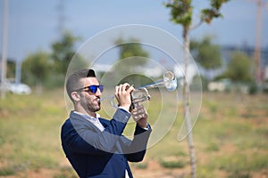 Handsome young businessman with a beard and a blue suit playing the trumpet. The man is a musician in his spare time and music is