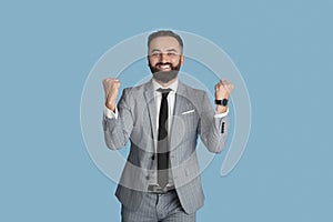 Handsome young businessman feeling excited and gesturing YES on blue studio background