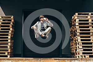 handsome young businessman floating in air in lotus pose and drinking coffee at industrial location in front of roller