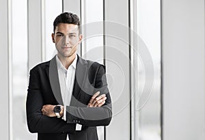 Handsome young businessman with folded arms in the office. Cheerful self confident man with crossed hands portrait